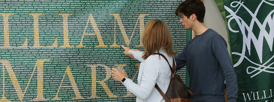 Two people point at the names of admitted students printed on a large sign